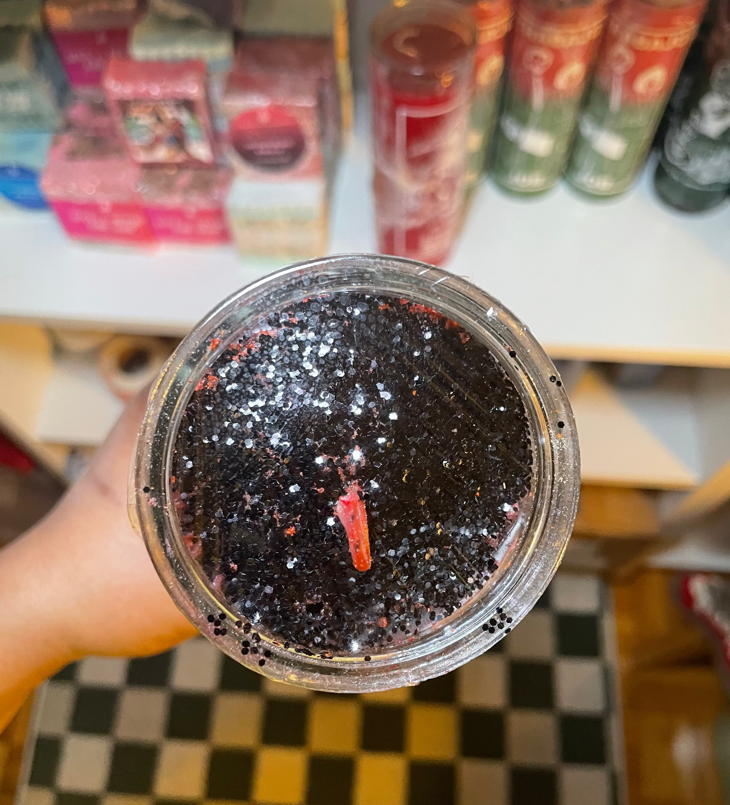 Hand holding a jar of black glittery substance with a store shelf in the background