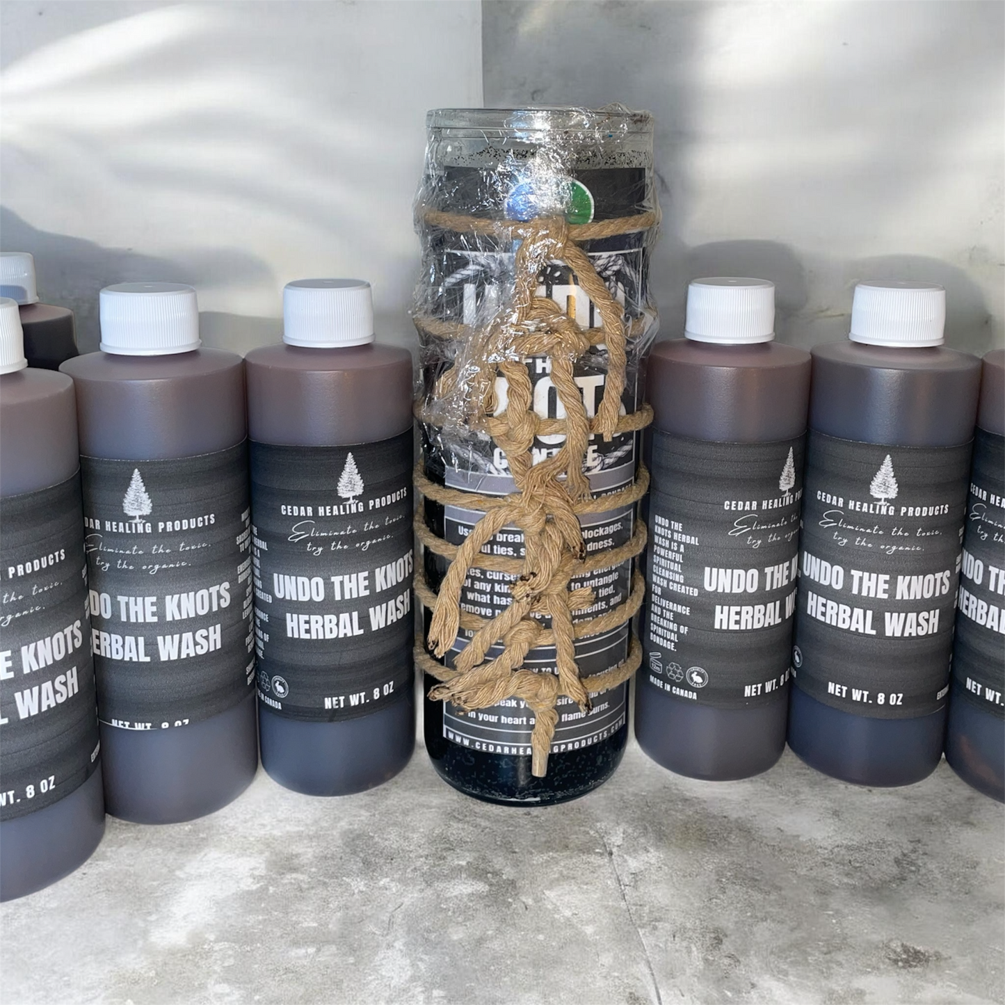 Bottles of 'Undo the Knots Herbal Wash' with a central bottle wrapped in rope on a gray surface.